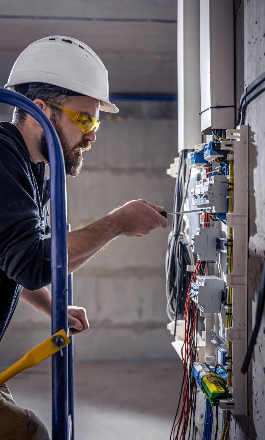 A male electrician works in a switchboard with an electrical connecting cable, connects the equipment with tools.